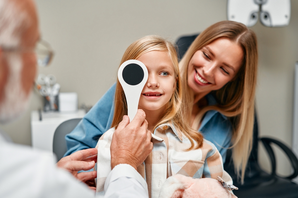 A young girl undergoes a vision screening while her parent provides support, guided by an optometrist. Early eye exams help detect refractive errors and developmental vision issues in children – Optometrist.