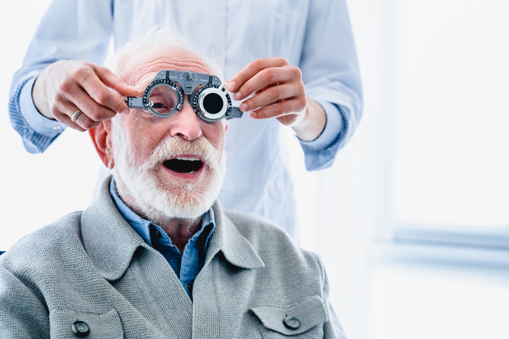Senior Man Receiving Trial Lens Refraction – Glasses Exams An older man smiles as the eye doctor adjusts a trial lens frame during his refraction test. This essential process helps identify the perfect prescription for new eyeglasses – Glasses Exams.