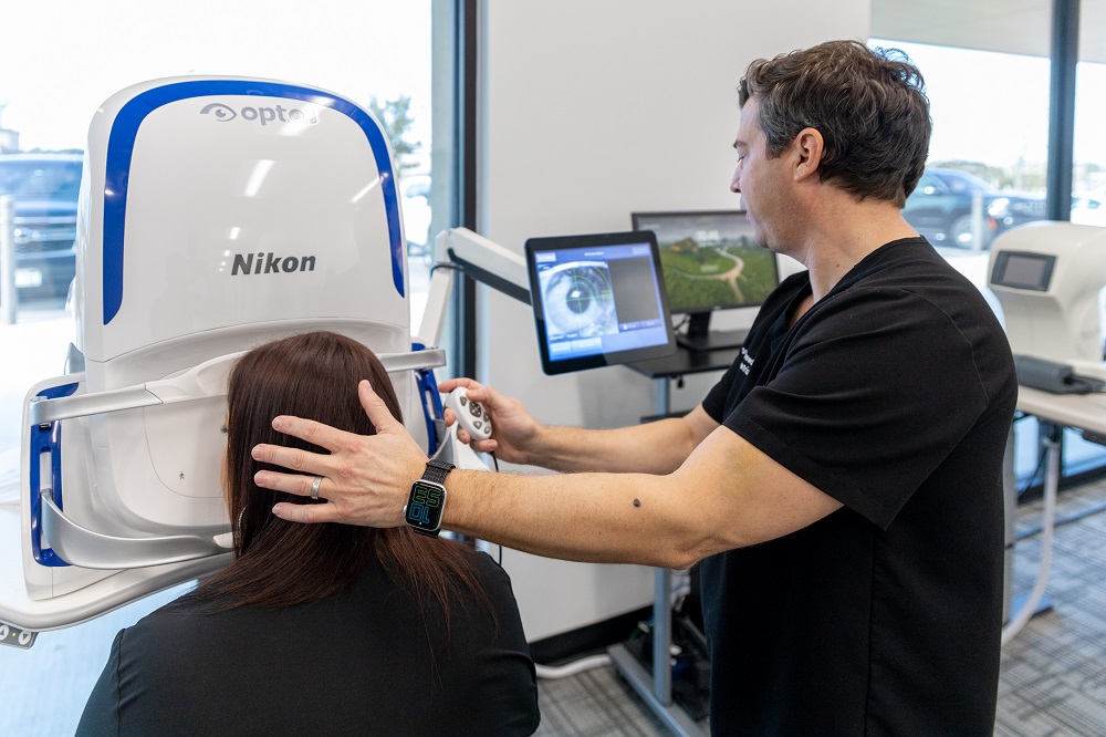 A healthcare professional guides a patient through a high-tech retinal imaging scan using a Nikon Optos machine. The detailed eye scan displayed on the monitor highlights the importance of early detection and diagnosis for patients experiencing blurry vision.
