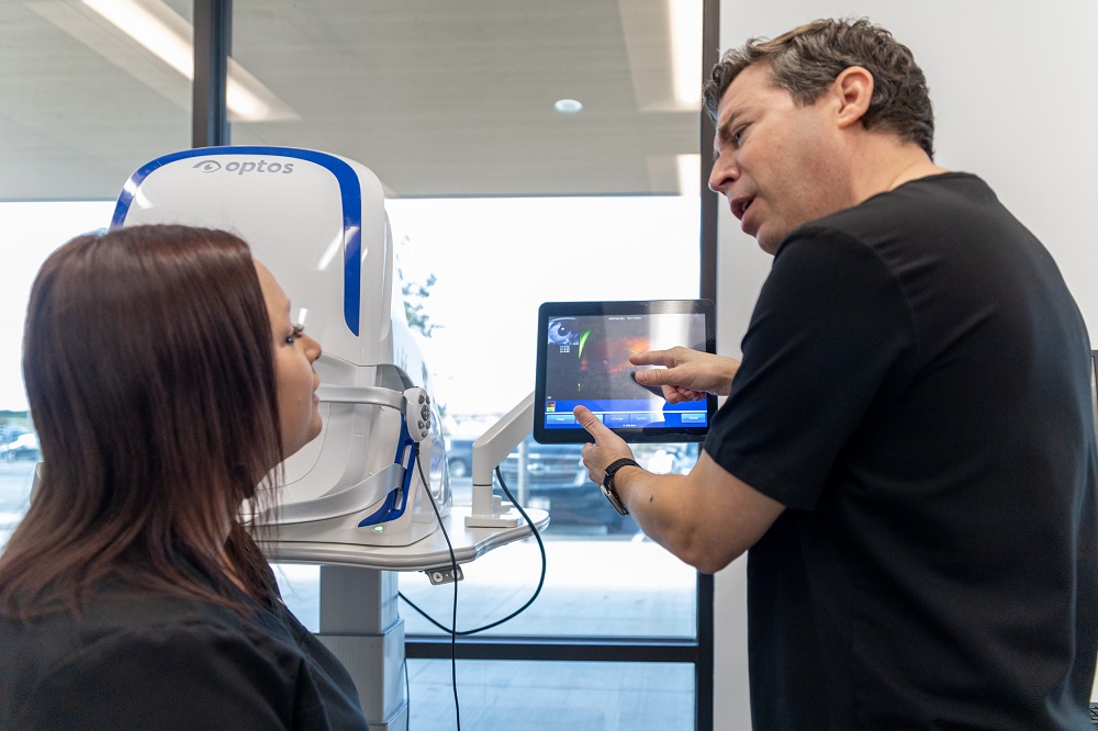 An optometrist reviews detailed retinal imaging results with a patient using a high-tech Optos scanning device. This consultation helps diagnose early signs of eye conditions and ensure long-term vision health – Optometrist.