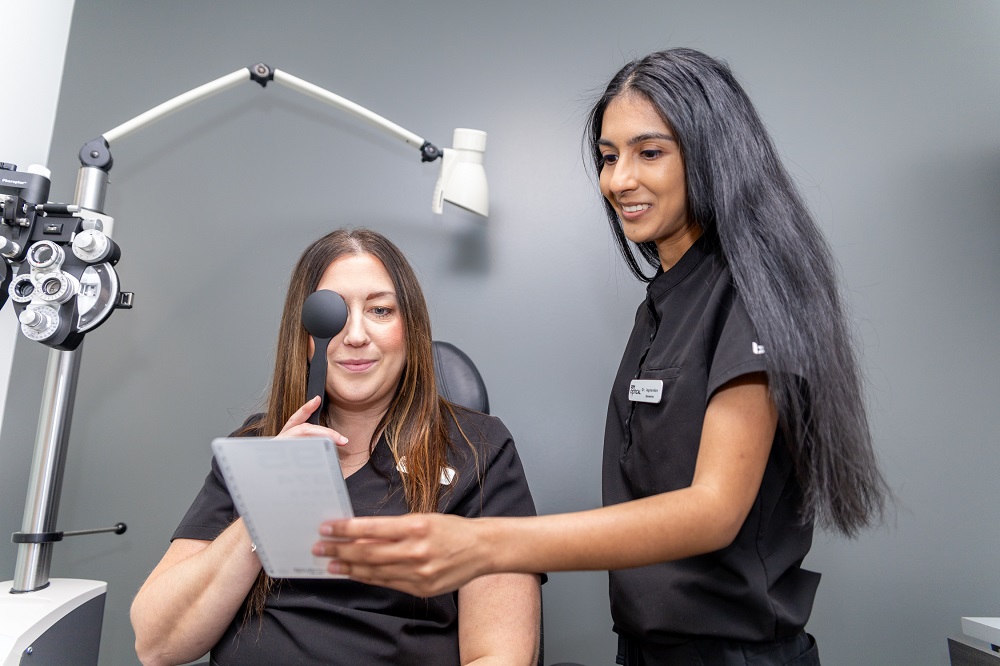 Patient Performing Vision Test with Eye Cover – Glasses Exams A patient covers one eye while reviewing a vision chart guided by an eye care professional. This step helps determine prescription accuracy and ensures the right glasses for optimal clarity – Glasses Exams.