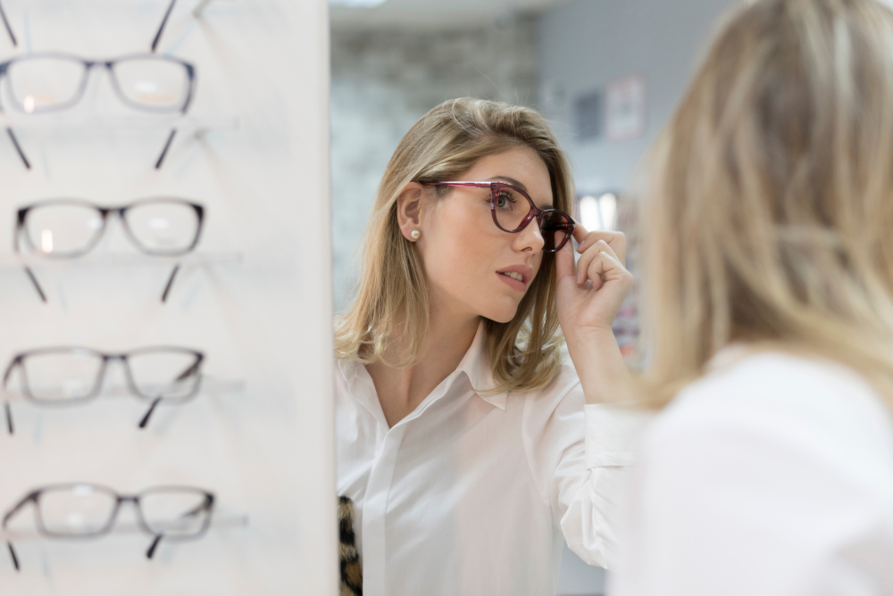 A customer tests out a pair of stylish eyeglasses while looking into a mirror, ensuring the perfect blend of comfort, clarity, and personal style – Eyeglasses.