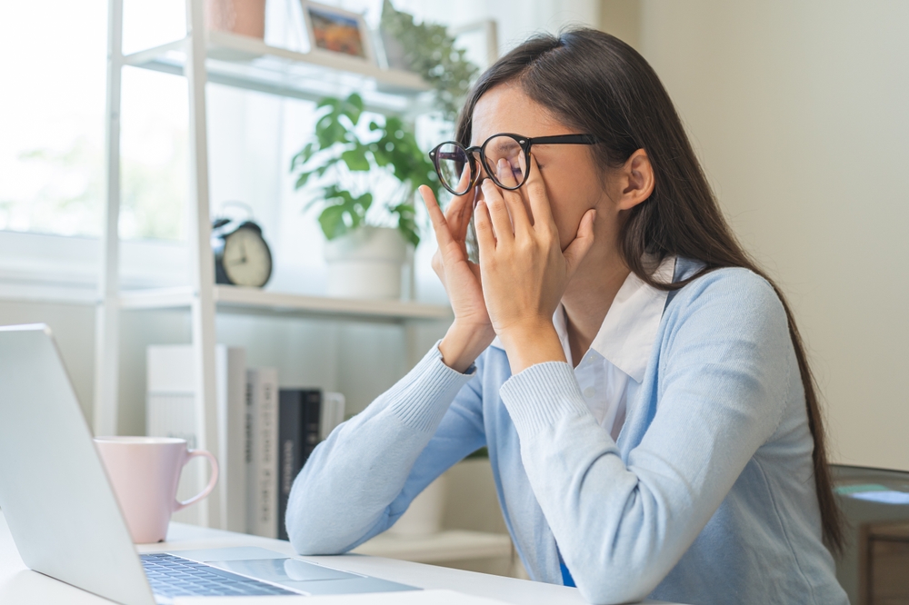 A woman rubs her eyes while working on her laptop, showing signs of digital eye strain or underlying ocular conditions. Identifying symptoms like dryness, irritation, or blurred vision early helps prevent progressive eye disease – Ocular Disease Management.
