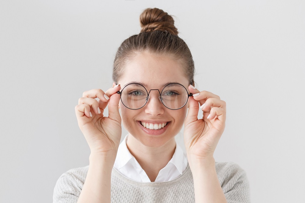 Happy Woman Trying On New Eyeglasses – Georgetown Eyeglasses A cheerful woman adjusts her new round eyeglasses, enjoying a clear, comfortable view after selecting the perfect pair for her daily needs. – Georgetown Eyeglasses
